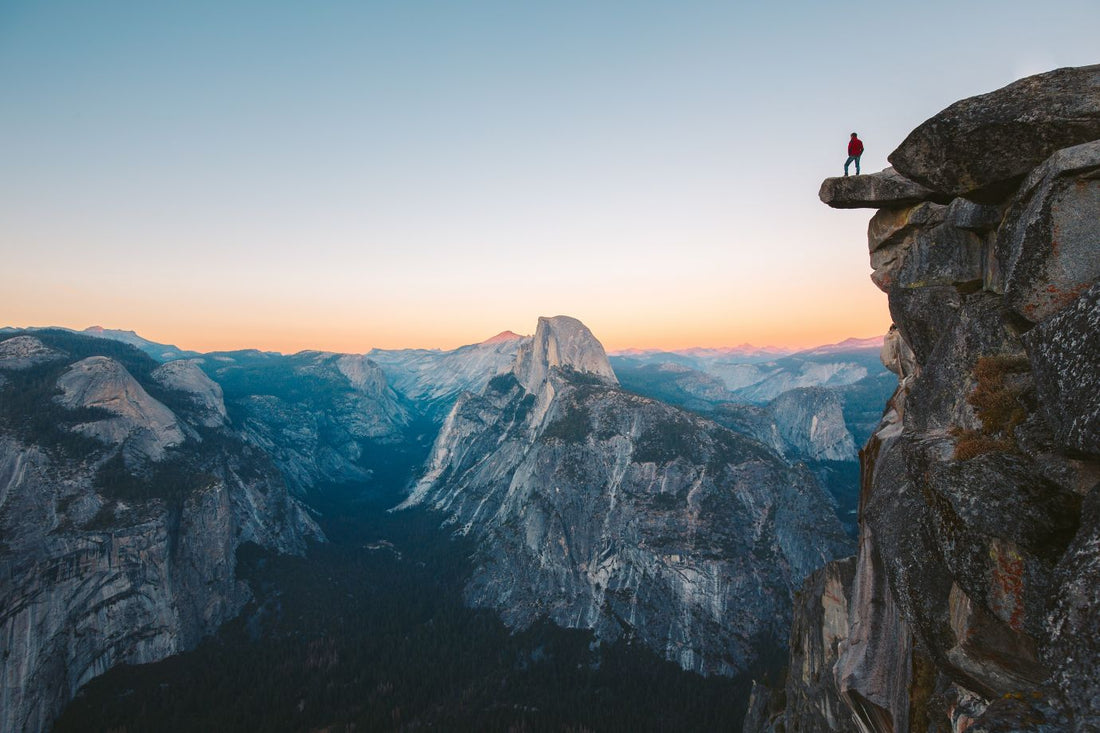 A fearless hiker is standing on an overhanging rock enjoying the view towards famous Half Dome at Glacier Point