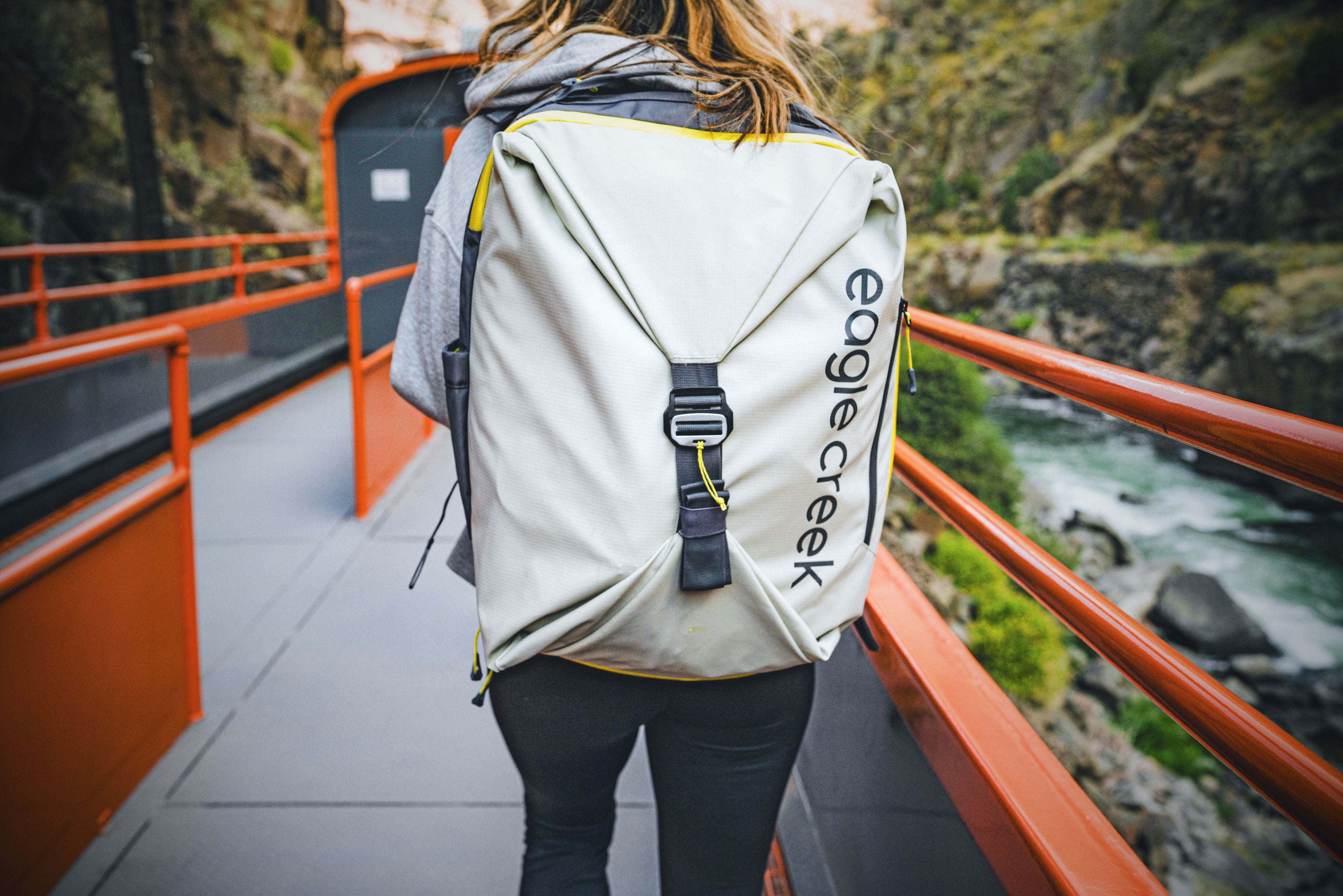 A woman walking on a bridge wearing an Eagle Creek travel backpack